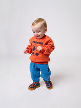 Load image into Gallery viewer, Child wearing an orange sweatshirt with text and blue pants on a white background