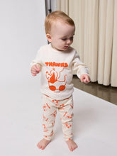 Load image into Gallery viewer, Baby wearing a white outfit with orange graphics and text, standing on a light surface.