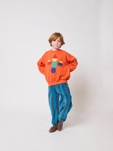 Load image into Gallery viewer, Child wearing an orange sweater with a colorful design and blue striped pants on a white background